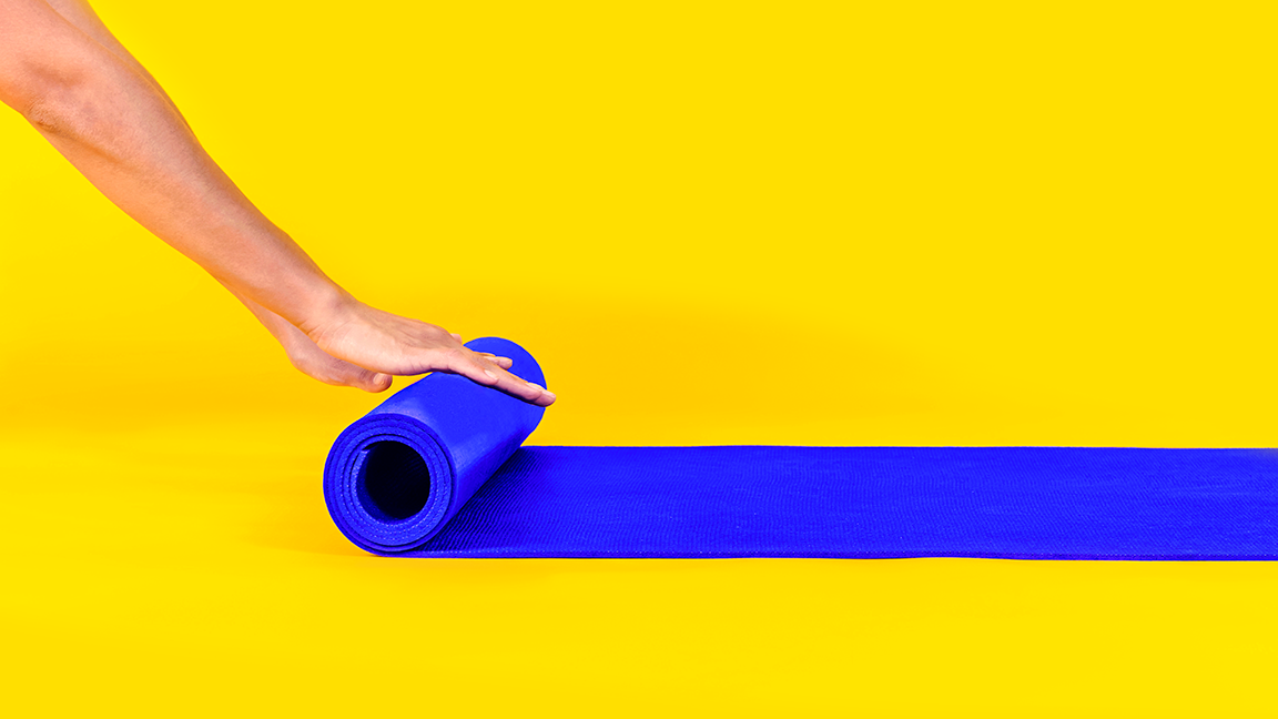 Woman hands doing rolling colored yoga mat on yellow background. Sport and healthy lifestyle concept