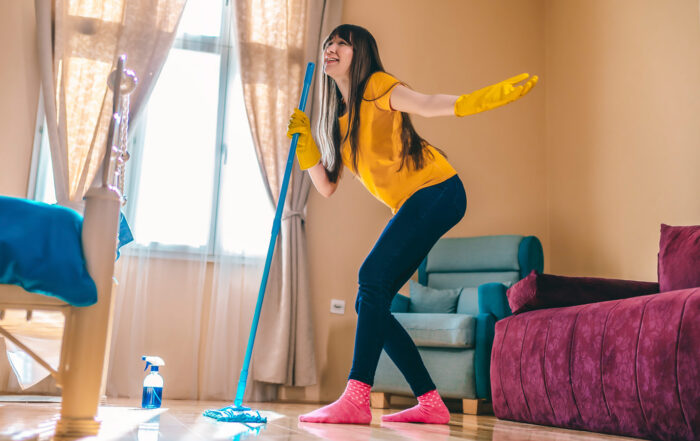 Happy woman cleaning home and having fun by singing at mop like on microphone