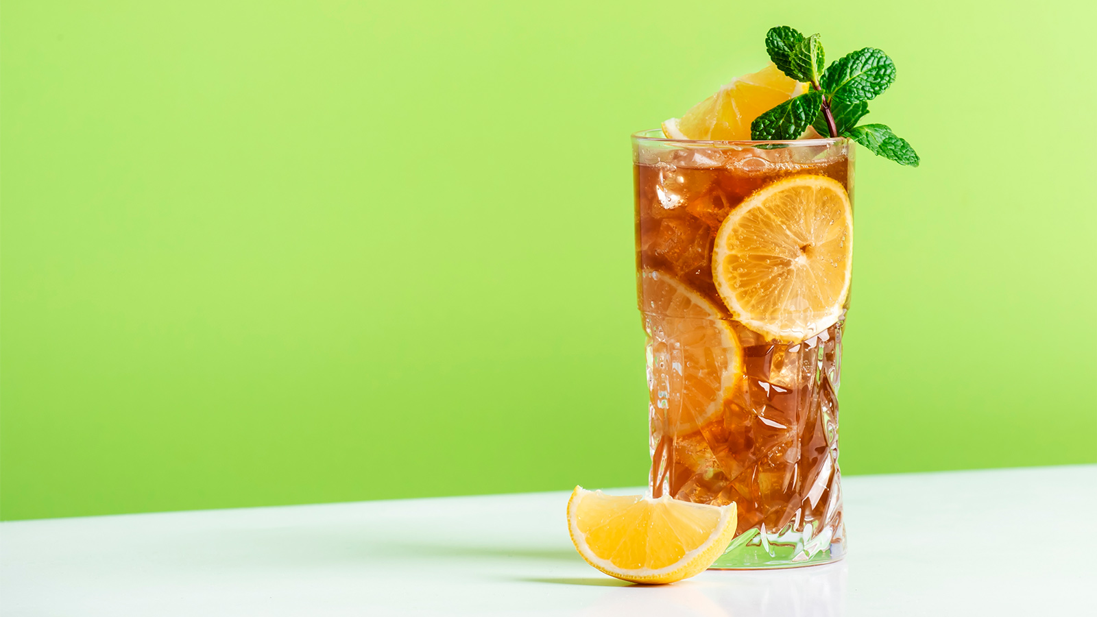 Glass of lemon iced tea with mint on green background