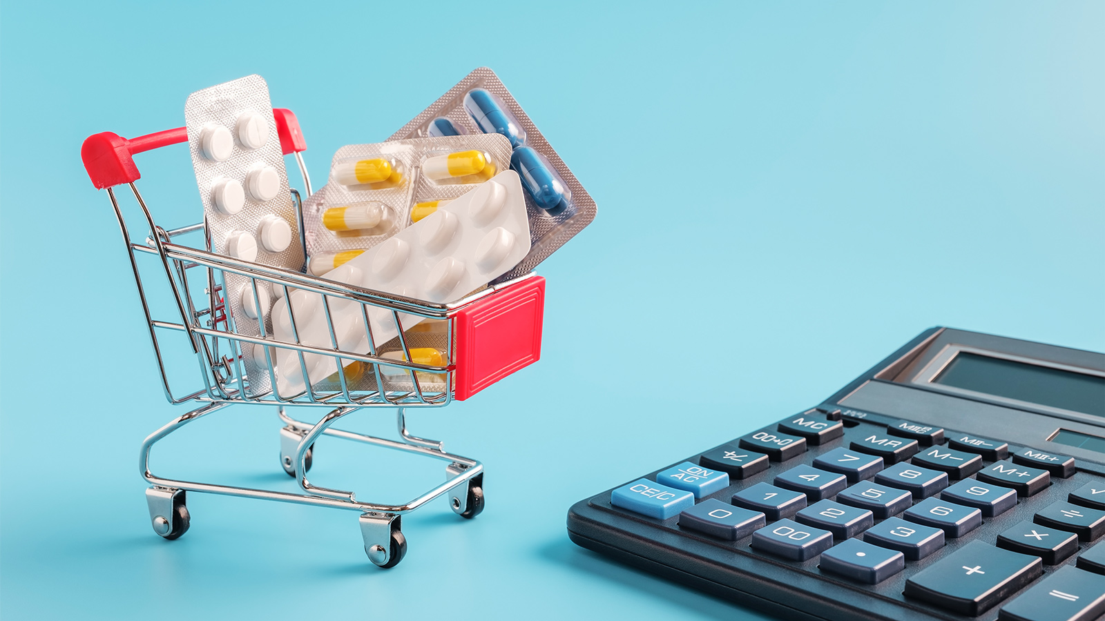 Mini shopping cart filled with medication and a calculator on baby blue background