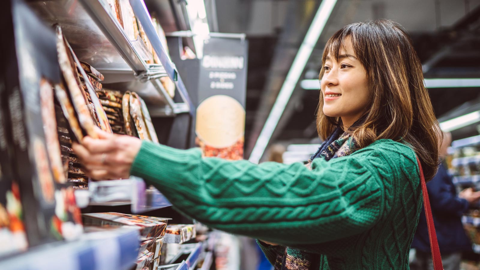 Young woman shopping for prepared meal in front of a refrigerator in supermarket.