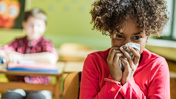 Student in a classroom blowing their nose into a tissue