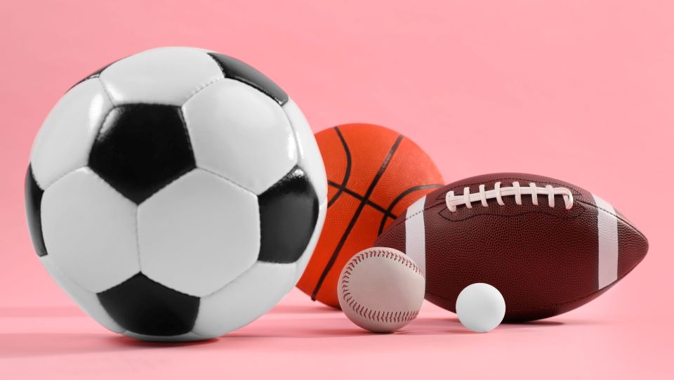 Many different sports balls on pink background